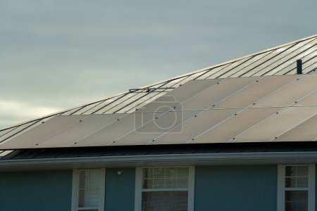 Standard american residential house with rooftop covered with solar photovoltaic panels for producing of clean electrical energy in suburban rural area. Concept of investment in autonomous home.