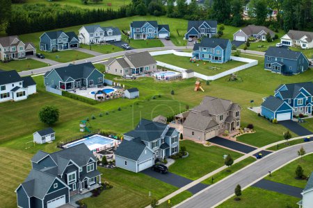 Aerial view of private residential houses in rural suburban sprawl area in Rochester, New York. Upscale suburban homes with large backyards and green grassy lawns in summer season.