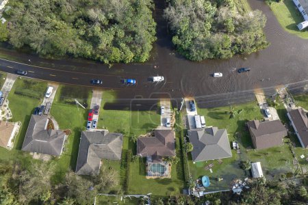 Flooded Florida road with evacuating cars and surrounded with water houses in suburban residential area. Consequences of hurricane natural disaster.