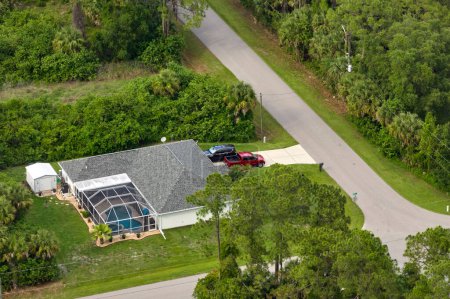 Aerial view of typical contemporary american private house with roof top covered with asphalt shingles and green lawn on yard.