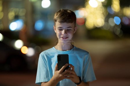 Happy teenage boy messaging on his cellphone outdoors at night.