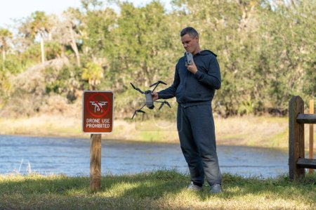 Operator is disappointed because he can not fly his quadcopter in national park no drone area. Man is unable to use his UAV near restriction notice sign.