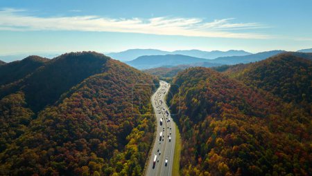 View from above of I-40 freeway route in North Carolina leading to Asheville thru Appalachian mountains with yellow fall woods and fast moving trucks and cars. Interstate transportation concept.