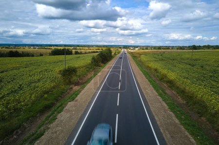 Vista aérea de la carretera interurbana entre campos agrícolas verdes con coches de conducción rápida. Vista superior desde el dron del tráfico por carretera.