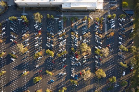 Vue aérienne de nombreuses voitures stationnées sur le parking avec des lignes et des marques pour les places de stationnement et les directions. Place pour les véhicules devant une épicerie.