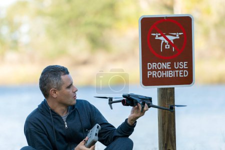 Man is sad that he is not allowed to fly his quadcopter state park no drone area. Operator is unauthorised to use UAS near restriction sign.