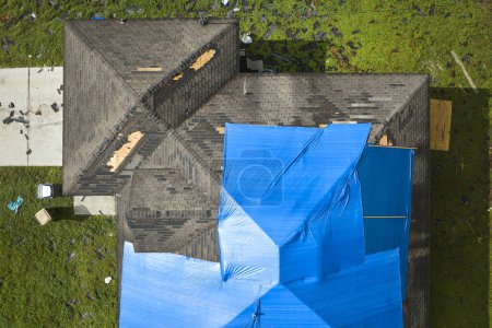 Vue aérienne du toit endommagé de la maison de l'ouragan Ian recouvert d'une bâche de protection bleue contre les fuites d'eau de pluie jusqu'au remplacement des bardeaux d'asphalte.