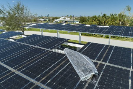 Failing of photovoltaic technology integrated in urban infrastructure. Hurricane wind damage to solar panels installed as shade roof over parking lot for parked electric cars.