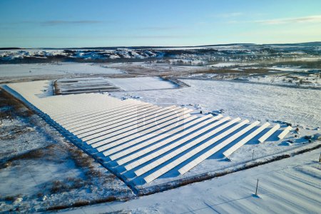 Aerial view of sustainable electrical power plant with solar photovoltaic panels covered with snow in winter for producing clean energy. Concept of low effectivity of renewable electricity in north.