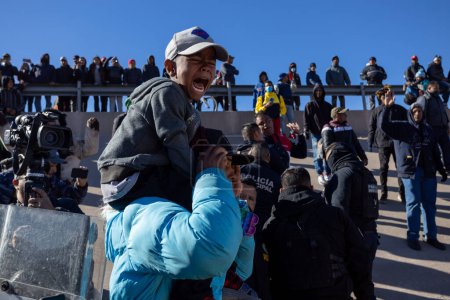 Photo for Juarez, Mexico, 11-27-2022: A migrant carries his son on his shoulders to leave the camp located on the border between Mexico and the United States, after being evicted but by the municipal police and the Mexican National Guard. - Royalty Free Image