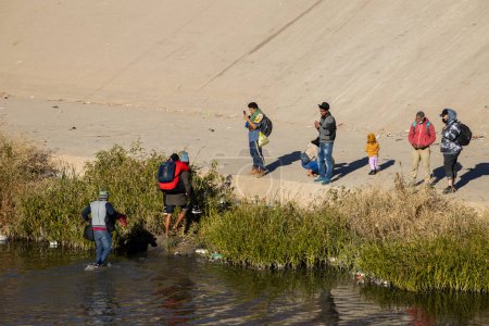 Foto de Juárez, México, 21-12-2022: cientos de migrantes esperan frente al muro para poder entregarse a la patrulla fronteriza en territorio americano, para solicitar asilo humanitario. - Imagen libre de derechos