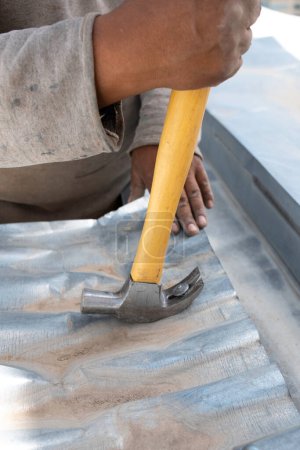 Foto de Trabajador quitando un clavo con un martillo de una plancha corrugada - Imagen libre de derechos