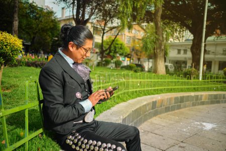 Foto de Un latino toma el sol mientras se pone al día con un amigo en su teléfono en la plaza - Imagen libre de derechos