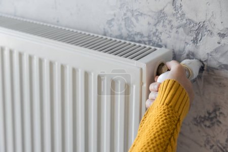 Foto de Male hand in yellow sweater adjusting comfort temperature in home by control gas heater. Energy efficiency or economy in winter concept - Imagen libre de derechos