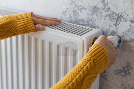 Téléchargez les photos : Man adjusting heating radiator or heater to install comfort temperature for energy efficiency and economy in winter. Concept of heating season - en image libre de droit