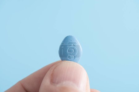 Mann hält blaue Pille Viagra in den Fingern auf blauem Hintergrund. Medizinisches Konzept der Männergesundheit, Medikamente für Potenz, Erektion, Behandlung der erektilen Dysfunktion Makroschuss