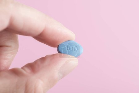 Man hold blue pill viagra in fingers on pink background. Medicine concept of men health, medication for potency, erection, treatment of erectile dysfunction Close up