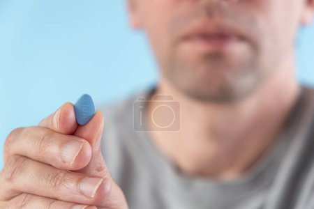 Photo for Man hold blue pill in fingers on blue background. Medicine concept of men health, medication for potency, erection, treatment of erectile dysfunction Macro shot - Royalty Free Image