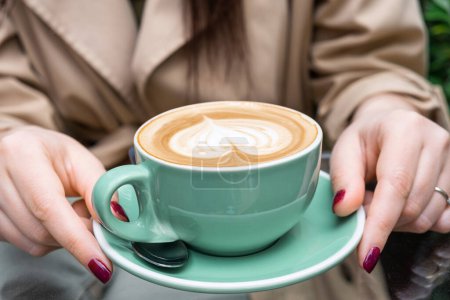 Photo for Cup of coffee cappuccino or latte in woman hands outdoors in coffee house or cafe. Classic heart shaped latte art on foam. Tasty hot drink - Royalty Free Image