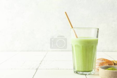 Photo for Glass of iced green matcha latte with a straw on white tile background. Cold summer drink - Royalty Free Image