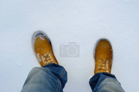 Top view of yellow boots in fresh snow. Winter season.