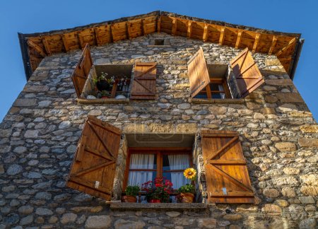 Photo for Old rural stone house in the Pyrenees with open wooden windows and precious pots. The light of the late afternoon sun beautifully illuminates the windows, shutters and stonework. - Royalty Free Image