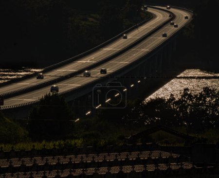 Photo for Highway bridge illuminated at twilight with the rias baixas below illuminated by the sun and the Taragoa cemetery below where you can see the crosses illuminated at sunset - Royalty Free Image