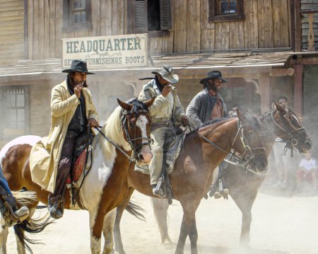 Foto de Tres forajidos vestidos con sombreros de vaquero y ropa montada en sus caballos listos para atacar - Imagen libre de derechos