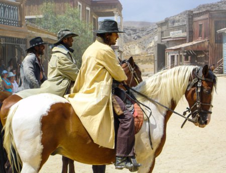 Foto de Tres forajidos vestidos con sombreros de vaquero y ropa montada en sus caballos listos para atacar - Imagen libre de derechos