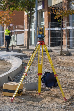 Total station with yellow tachymeter or theodolite with tripod to measure the land surface of the construction zone with the surveyor in the background calculating data and elevations