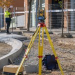 Total station with yellow tachymeter or theodolite with tripod to measure the land surface of the construction zone with the surveyor in the background calculating data and elevations