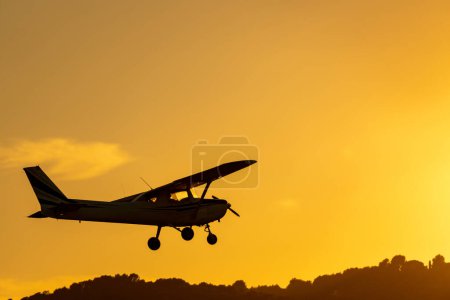Photo for Silhouette of small propeller plane landing or taking off on the runway backlit under a yellow sun with the mountain below at sunset in Sabadell airport. - Royalty Free Image