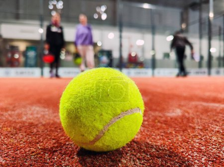 Photo for Detail shot of a paddle ball on the floor of the indoor paddle tennis court and three player friends in the background of the court - Royalty Free Image