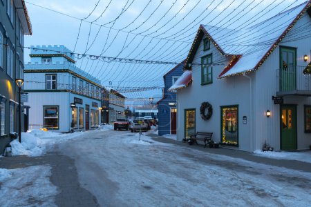 Photo pour Rue avec des magasins classiques dans la vieille ville de Selfoss illuminée avec des lumières de Noël et des ornements et la rue avec de la neige et de la glace au coucher du soleil. - image libre de droit