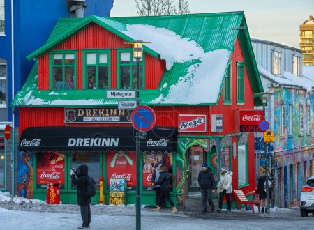 Foto de Típica casa de hielo rojo con techo verde con placas de nieve de un pintoresco bar Reykjavik lleno de afiches de bebidas y una casa de artista llena de pinturas y graffiti - Imagen libre de derechos