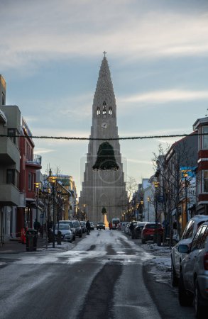 Photo for Front of Hallgrimskirkja church illuminated by the first light of dawn and lit street lamps from Skolavordustigur street icy with ice sheets on the sidewalks and ground. - Royalty Free Image