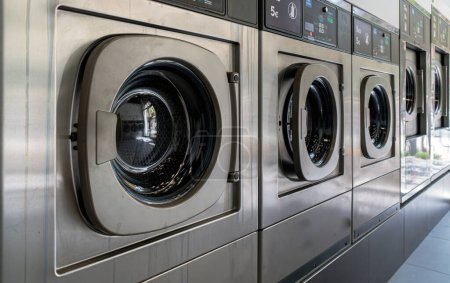 Téléchargez les photos : Lave-linge dans une blanchisserie urbaine pour laver et sécher les vêtements, les draps et les nappes en rangée avec les portes fermées - en image libre de droit