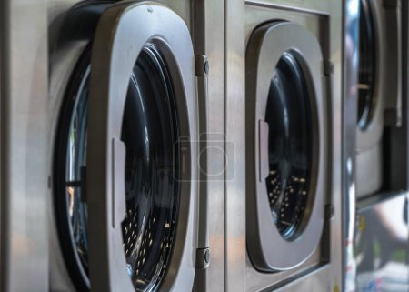 Téléchargez les photos : Lave-linge dans une blanchisserie urbaine pour laver et sécher les vêtements, les draps et les nappes en rangée avec une porte semi-fermée - en image libre de droit