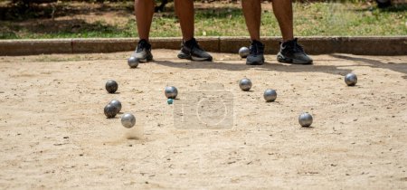 Photo for Metal ball from the game of petanque approaching the bowling alley bouncing off the sandy ground raising dust from a petanque court on a sunny day with opposing players in the background - Royalty Free Image
