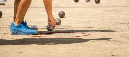 Photo for Hand of young sporty woman in sports shoes catching metal petanque ball to compete in qualifying game playing petanque game on a sunny day on a sandy ground petanque court - Royalty Free Image
