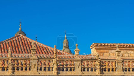 Spitze des kunstvollen Steinzauns des Kreuzganges der Universität von Salamanca und orangefarbenes Ziegeldach