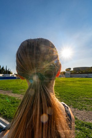 Photo for A young runner, tanned with her long brown hair, looking towards the sun bright with the evening rays for inspiration, serenity and peace. - Royalty Free Image