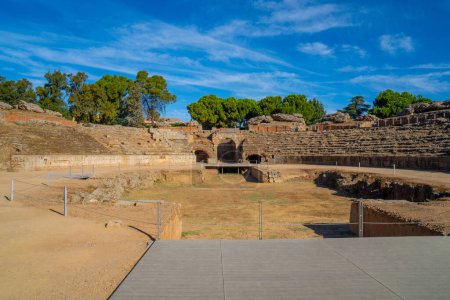 Téléchargez les photos : Vue de la passerelle en bois de l'arène de l'Amphithéâtre romain de Mérida éclairée par la lumière de l'aube créant des ombres sur ses stands avec l'entrée voûtée en arrière-plan. - en image libre de droit