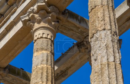 Photo for Detail of the ornate moldings on the Corinthian order columns and capitals of the well-preserved Roman Temple of Diana under a clear blue sky and doves perched on its beams. Merida. - Royalty Free Image