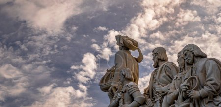 Foto de Perfil oriental con esculturas de piedra caliza y Henry el Navegante sosteniendo en su mano un barco del Monumento a los Descubrimientos de Lisboa con un espectacular cielo azul nublado al atardecer. - Imagen libre de derechos