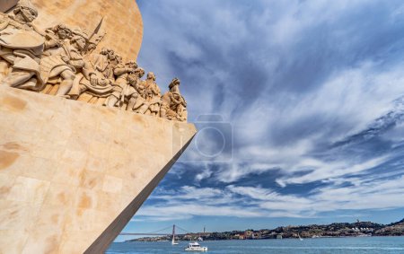 Western profile of the Monument of Discoveries in Lisbon, Portugal, Europe, with sailboats and boats sailing on the Tagus River and the 25 de Abril Bridge in the background.