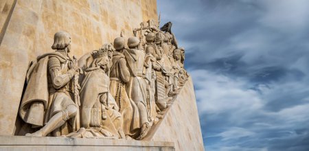 Blick von unten auf das westliche Profil des Monuments mit Kalksteinskulpturen auf die Entdeckungen in Lissabon, Portugal, unter wolkenblauem Himmel mit horizontalem Kopierraum.
