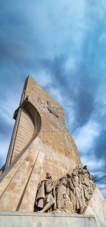 View from below of the western profile of the limestone Monument to the Discoveries in Lisbon, Portugal, under a cloudy blue sky with copy space.