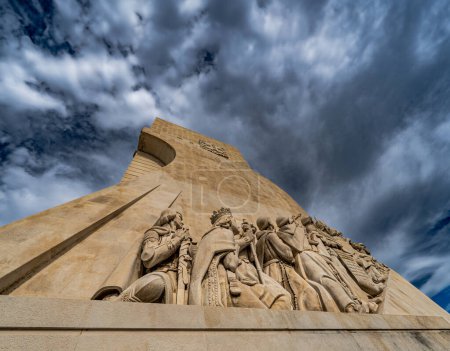 Blick auf die Westseite der Kalksteinskulpturen der Pioniernavigatoren am Monument der Entdeckungen in Lissabon, Portugal, unter einem dramatisch bewölkten blauen Himmel.