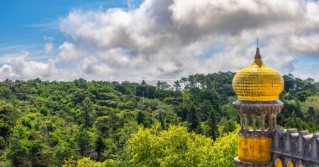 Wide-angle exterior view of the watchtower with dome decorated with yellow tiles of the Pena Palace, under a sunny cloudy blue sky, with the leafy Sierra de Sintra below on the horizon. Portugal.